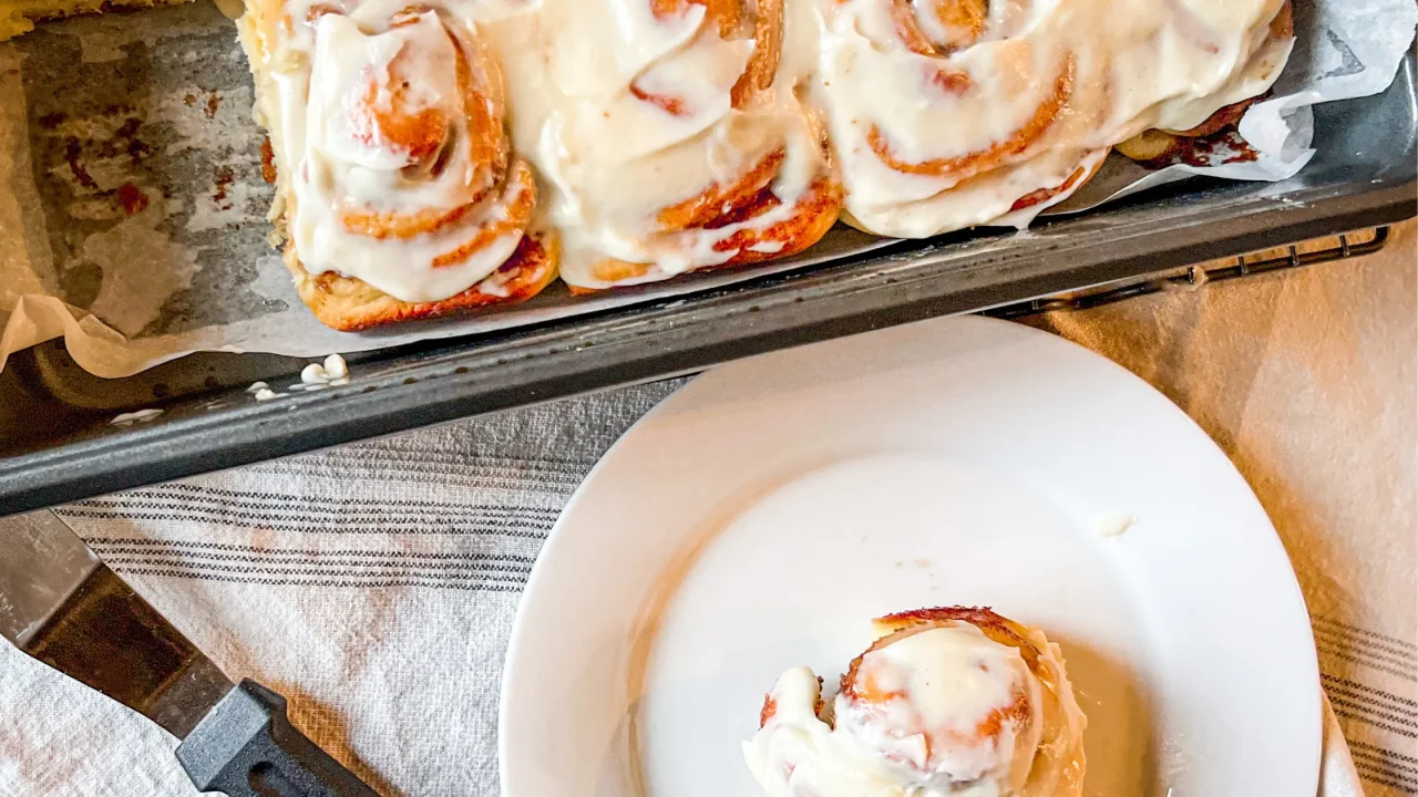 plate with a partially eaten homemade cinnamon roll on it next to a pan of baked cinnamon rolls