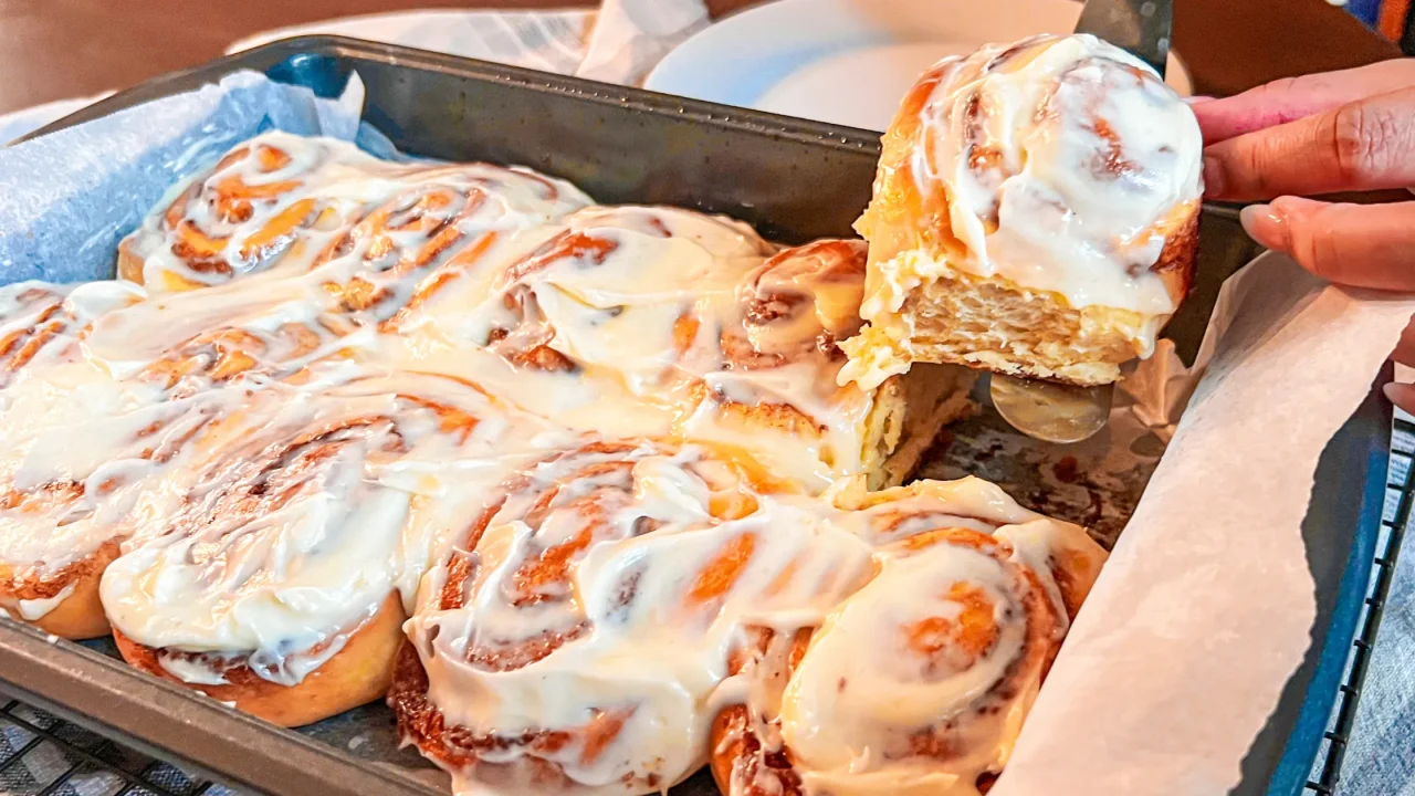 taking a homemade cinnamon roll out of a pan after baking