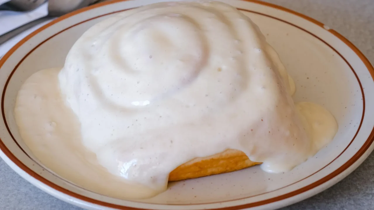 side view of a large cinnamon roll covered in frosting at vidlak's brookside cafe