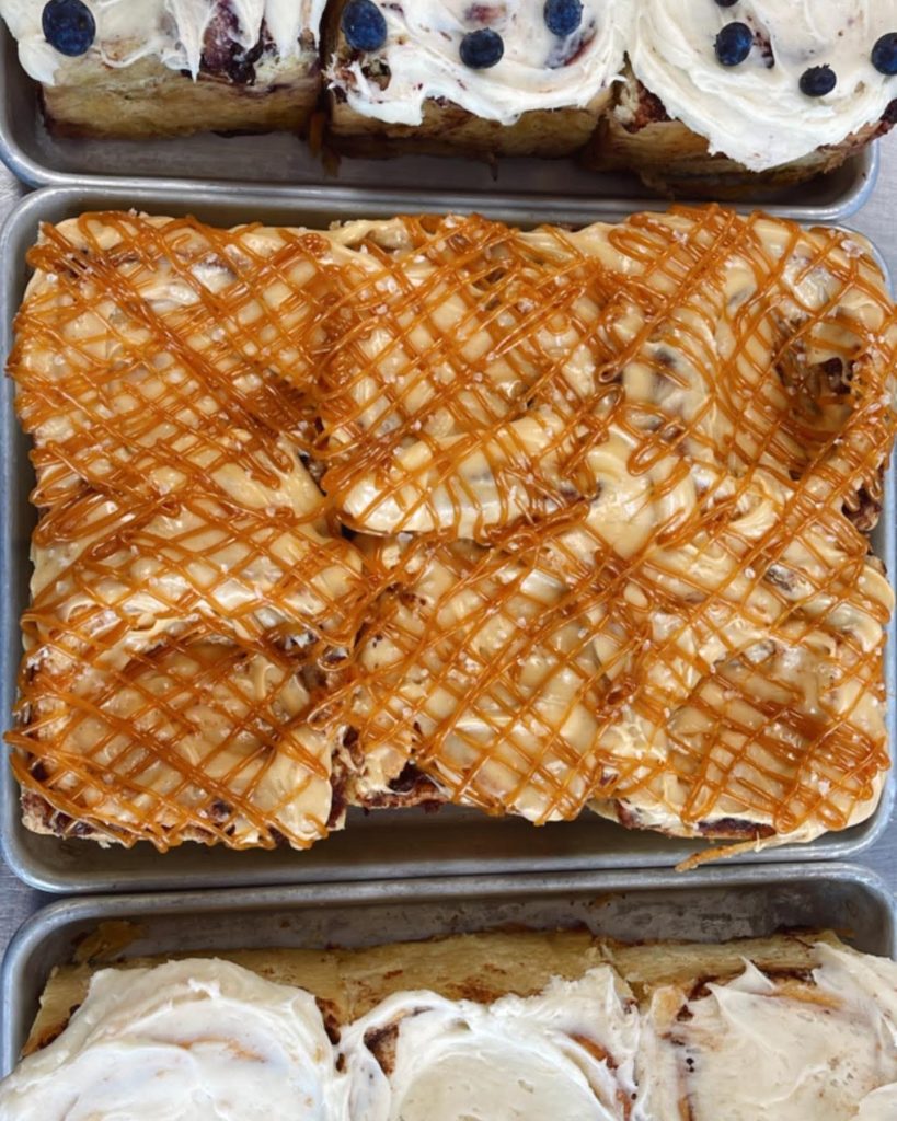 a catered affair a pan of caramel drizzled cinnamon rolls on a butcher block table