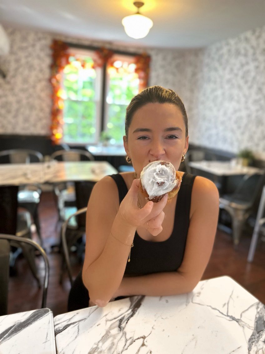 a young women in a black top is eating a cinnamon roll