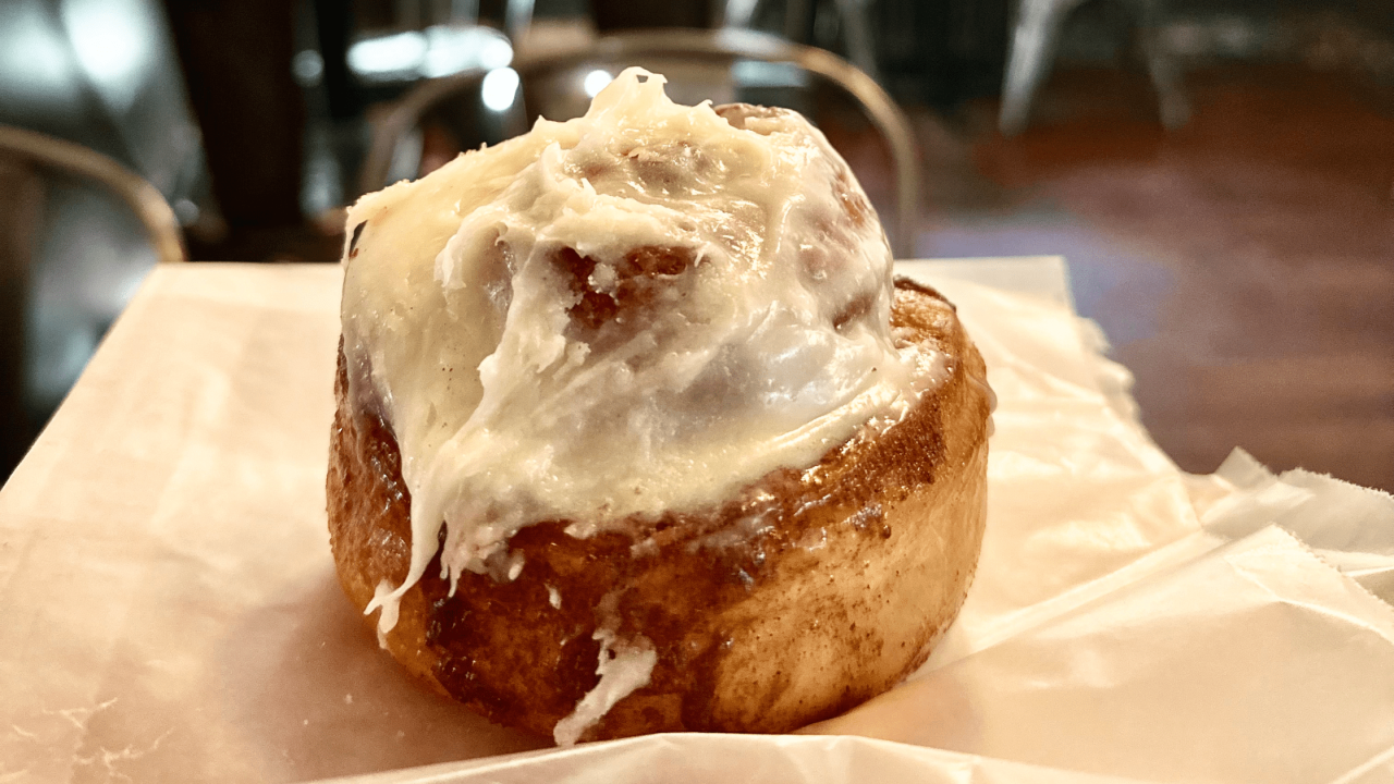 a creamy cinnamon roll on a plate that is sitting on a table in a bakery in New Jersey.